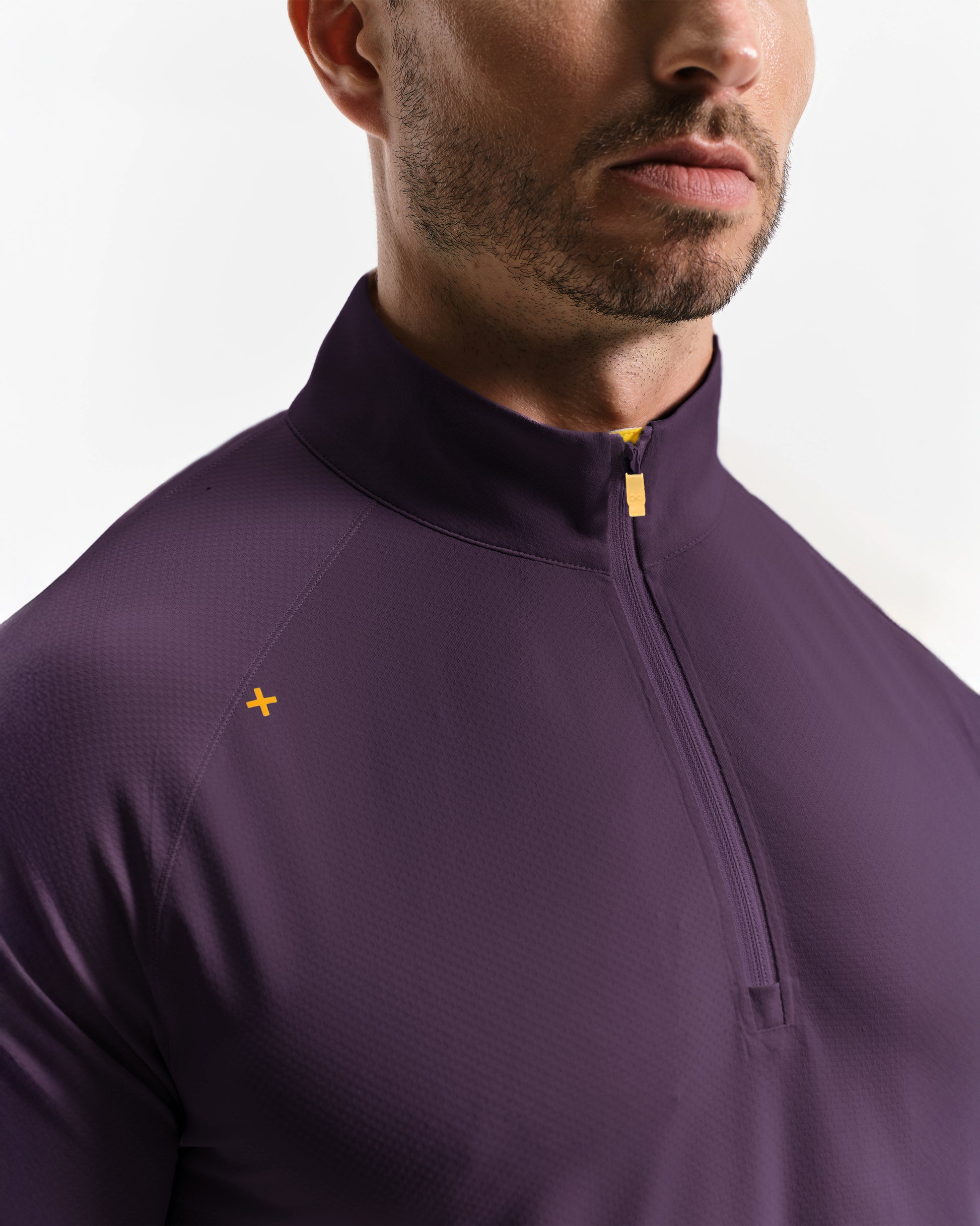 Close-up of a person wearing a purple quarter-zip shirt with a small yellow logo on a white background